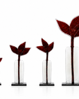 Four clear glass bud vases with black bases, arranged in ascending size order. Each vase contains a dark red, textured glass bud with three pointed leaves, set against a clean white background.