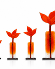 Four glass sculptures shaped like stylized flowers, arranged in ascending size order on a white background. Each vase has a translucent orange and red flower head with a clear glass neck and a black rectangular base.