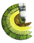 A crescent moon-shaped glass pendant featuring a green and black striped outer layer, a bright yellow center, a textured metallic gold inner crescent, and a stylized white, gray, and black face profile on the right side.