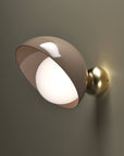 A versatile and vibrant lighting design from the Aurora Collection by Italamp featuring brushed gold accents, white glass diffuser, and retro-inspired finishes. A close up of taupe finish wall sconce with brushed brass finish detailing