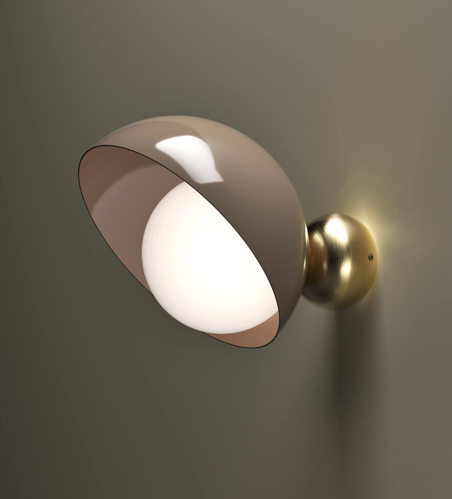 A versatile and vibrant lighting design from the Aurora Collection by Italamp featuring brushed gold accents, white glass diffuser, and retro-inspired finishes. A close up of taupe finish wall sconce with brushed brass finish detailing