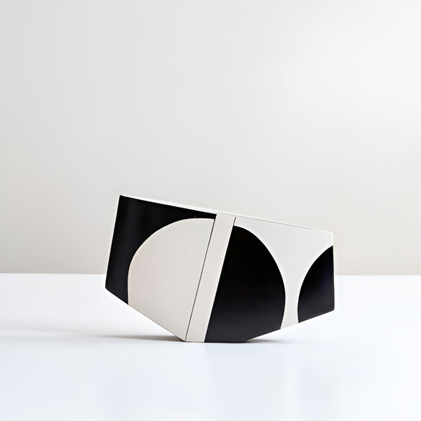 A modern geometric hand painted vase with a bold black and off-white abstract pattern, standing on its side on a clean white surface against a light gray background.