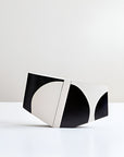 A modern geometric hand painted vase with a bold black and off-white abstract pattern, standing on its side on a clean white surface against a light gray background.