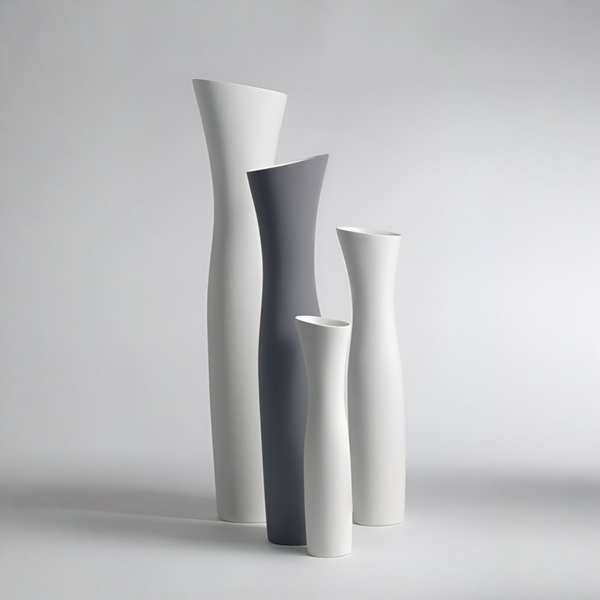 Four sculptural ceramic vases in minimalist curved shapes, including two tall white vases, one tall dark gray vase, and one short white vase, arranged on a light gray studio background.