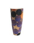 A tall, tapered ceramic vase with a warm beige background and a pattern of large hand-painted circles in purple, blue, black, and orange, set against a plain white background.