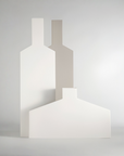 Three minimalist geometric wall art panels in white and light gray, arranged in a layered composition against a soft light gray studio background.