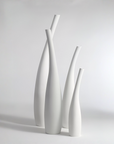 Four minimalist white ceramic vases of varying heights and neck widths, arranged together on a light gray studio background.