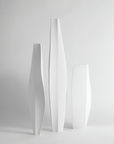 Three minimalist white ceramic vases of different heights with organic, flowing curves, arranged on a light gray surface against a neutral light gray background.