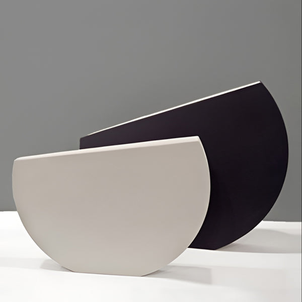 Two modern semi-circular ceramic vases in matte off-white and matte black, displayed against a neutral gray background by Kose Milano, available at Spacio in India. 