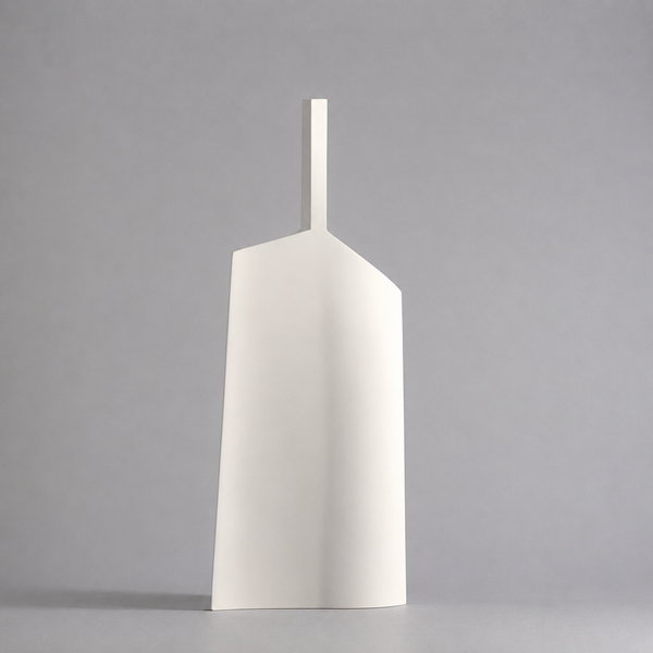 A minimalist white ceramic vase with a unique geometric, shield-like silhouette and a short cylindrical neck, standing on a neutral gray surface against a matching gray background.