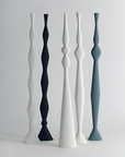Five sculptural decorative vase-like stems in matte white and muted blue-gray tones, arranged upright on a light gray studio background.