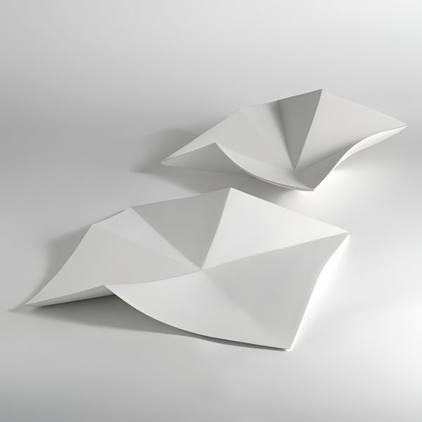 Two abstract white geometric platters with folded, faceted surfaces displayed on a light gray studio background.