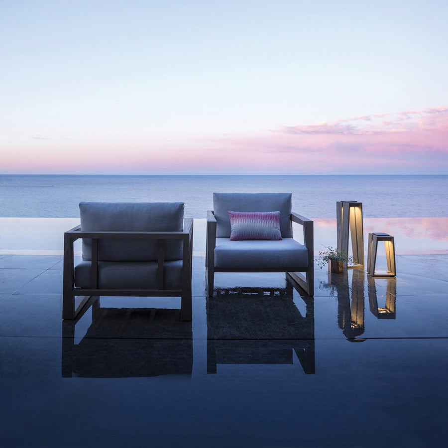 Two chairs and a Les Jardins LJ Solar Lantern SKAAL Tink120 Small 500L Duratek sitting on a concrete slab in front of the ocean, creating a Scandinavian modernism outdoor oasis.