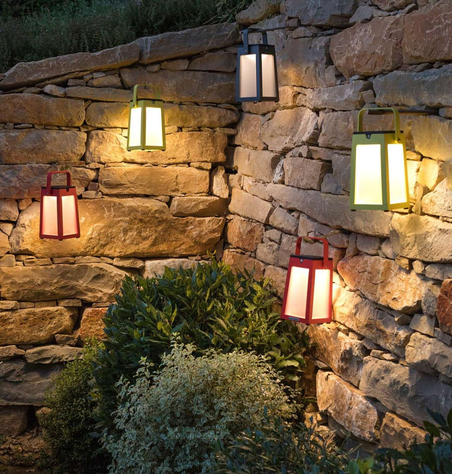 A group of Les Jardins outdoor solar lanterns hanging on a stone wall, providing portable and ambient lighting.