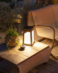 A wooden table with a Les Jardins Solar Lantern Tinka Tink138 300L Space Grey and wicker chairs on a deck, creating a cozy atmosphere with ambient lighting.