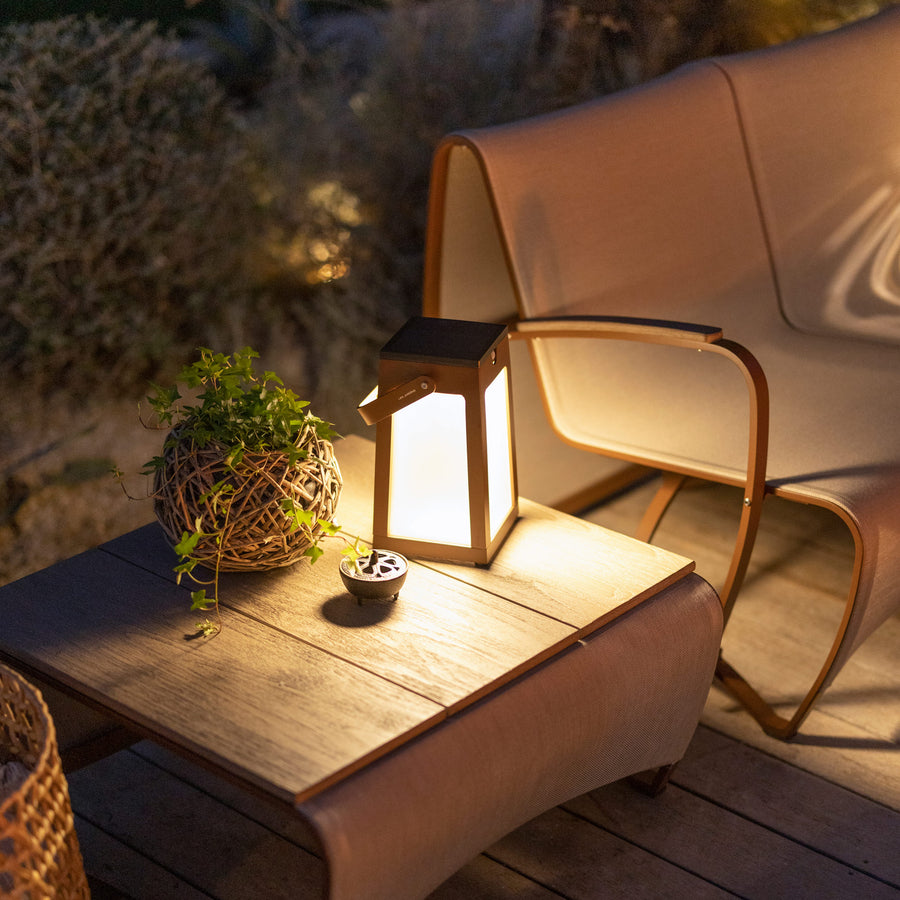 A wooden table with a Les Jardins Solar Lantern Tinka Tink138 300L Space Grey and wicker chairs on a deck, creating a cozy atmosphere with ambient lighting.