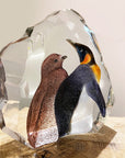 Tilted Back look of Maleras Crystal Sculpture King Penguin With Baby on wooden surface with flowers in back ground for modern interiors available at Spacio India from the Sculptures and Art Objects Collection.