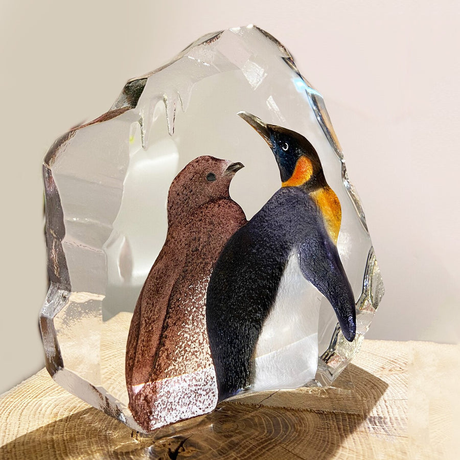 Tilted Back look of Maleras Crystal Sculpture King Penguin With Baby on wooden surface with flowers in back ground for modern interiors available at Spacio India from the Sculptures and Art Objects Collection.