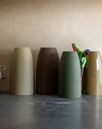 Four extra large planters of different colors in FRP arranged against a beige wall with a person interacting with one of them, available at Spacio retail stores in Mumbai & Kolkata. 