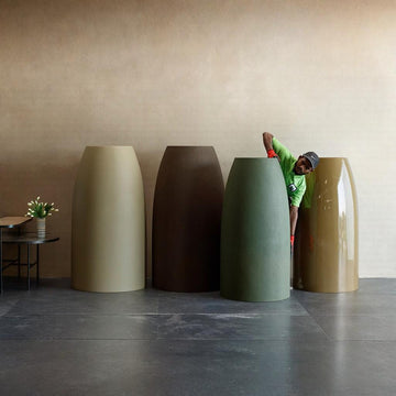 Four extra large planters of different colors in FRP arranged against a beige wall with a person interacting with one of them, available at Spacio retail stores in Mumbai & Kolkata. 