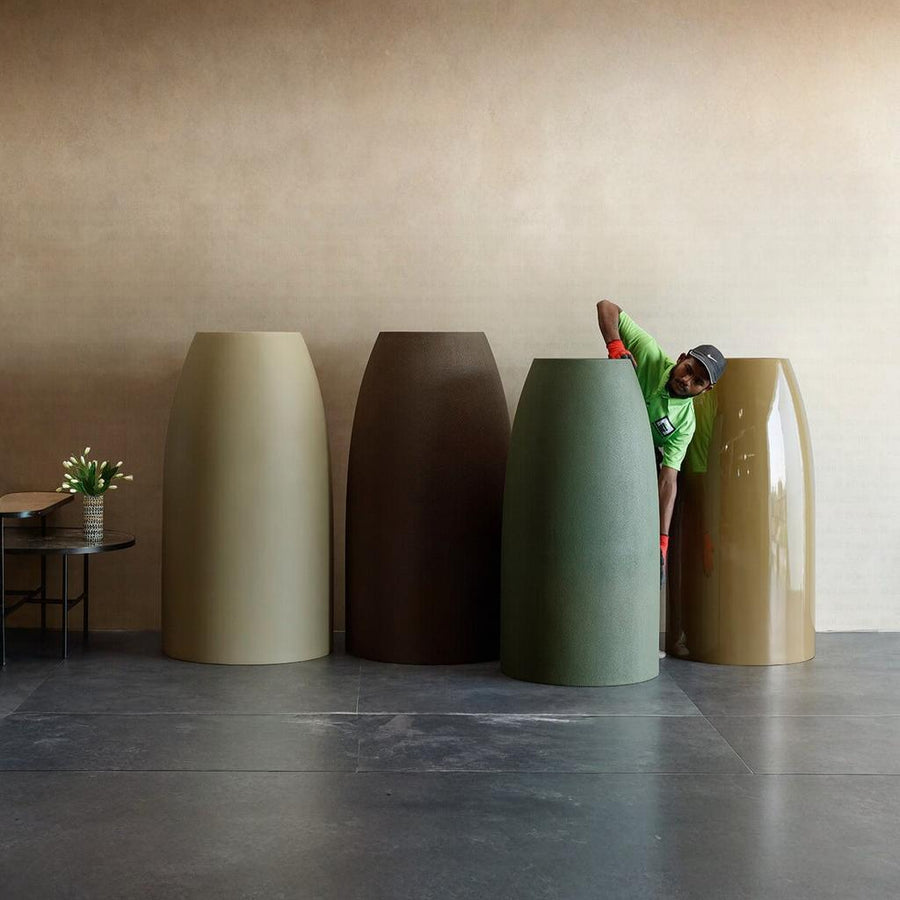 Four extra large planters of different colors in FRP arranged against a beige wall with a person interacting with one of them, available at Spacio retail stores in Mumbai & Kolkata. 