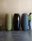 Three extra large planters of different colors (green, black, blue) with a person interacting with one of them in a minimalistic room, available at Spacio retail stores in Mumbai & Kolkata. 