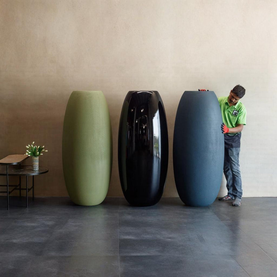 Three extra large planters of different colors (green, black, blue) with a person interacting with one of them in a minimalistic room, available at Spacio retail stores in Mumbai & Kolkata. 