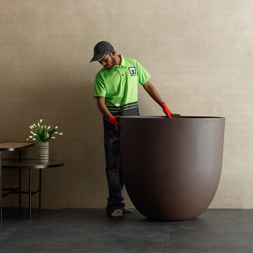 Person in a green shirt and cap moving a extra large planter in a room with a beige wall, available at Spacio retail stores in Mumbai & Kolkata. 