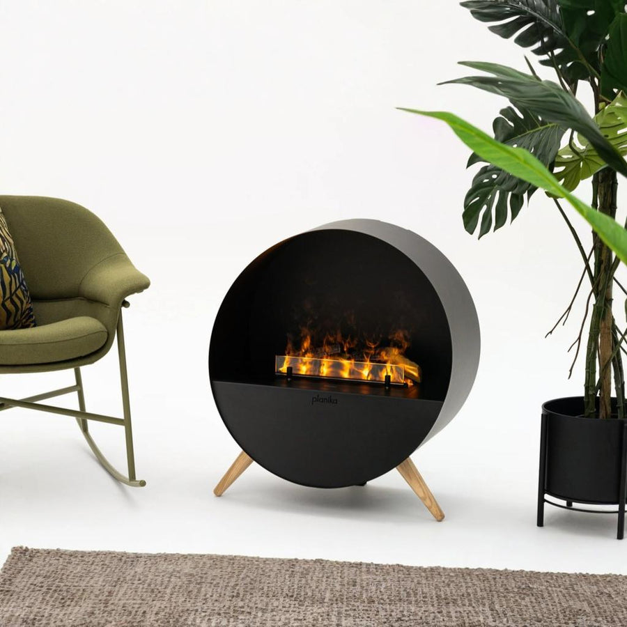 Modern artificial water vapour fireplace with flames, green chair, and plant on a white background available at Spacio retail stores in India. 