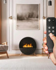 Hand holding a remote control with a modern living room in the background featuring a free standing artificial water vapour fireplace from Planika available at Spacio retail stores in India. 
