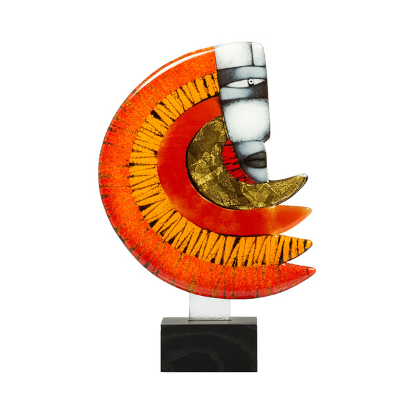 A modern abstract glass sculpture featuring a crescent moon and stylized face motif, mounted on a white vertical bar with a black marble base. The glass has vibrant orange and red gradients, textured black lines, a gold leaf pattern, and a white face with black details, set against a plain white background.