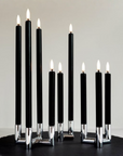 A set of mini ulta slim black taper candles with silver metal bases and white flame tips, arranged on a round black surface against a light gray background.