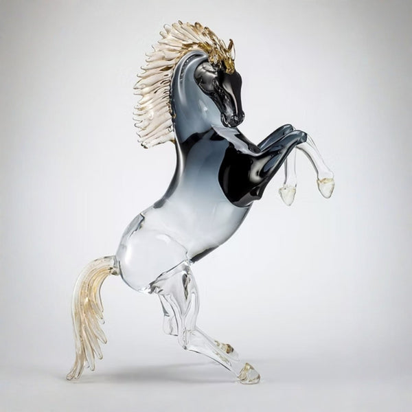 A Murano glass sculpture of a rearing horse with a black and smoky gray body, a white mane, and gold accents on the head and mane, set against a light gray background.