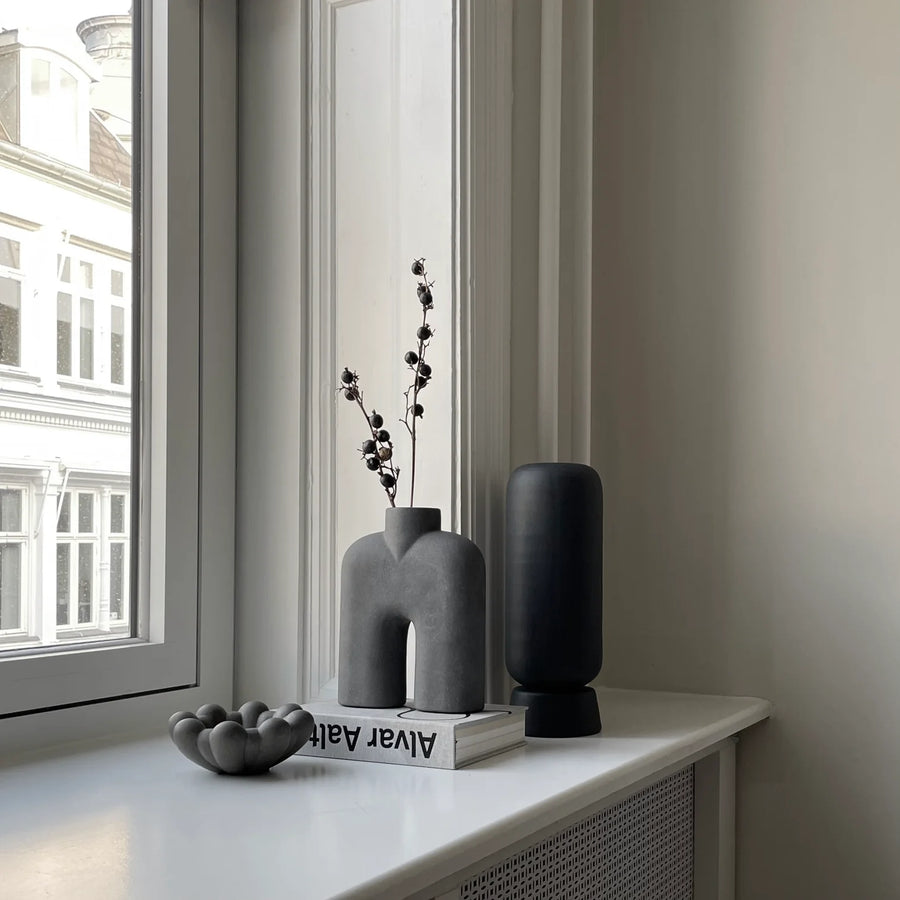 A window sill adorned with a 101Cph Cobra Tall Mini Dark Grey 211034 vase, displaying a beautiful flower.