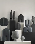 A group of black and white vases, including the 101Cph Cobra Tall Mini Dark Grey 211034 by 101 Copenhagen, displayed on a table.