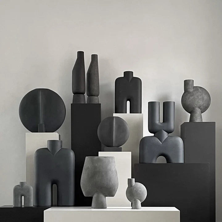 A group of black and white vases, including the 101Cph Cobra Tall Mini Dark Grey 211034 by 101 Copenhagen, displayed on a table.