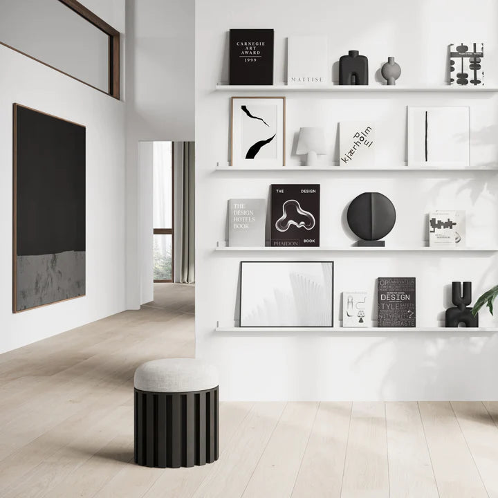 A white and black living room with shelves adorned with quirky vases, showcasing the sleek and elegant 101Cph Cobra Double Mini Black 203025. The space also features a stylish black stool for added seating options.