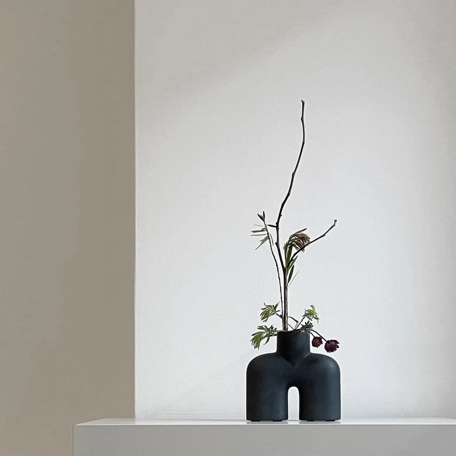 A quirky black vase, the 101Cph Cobra Uno Mini Black 203024 from 101 Copenhagen, gracefully adorns a pristine white wall.