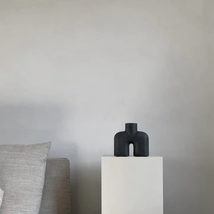 A quirky black vase, the 101Cph Cobra Uno Mini Black 203024 by 101 Copenhagen, is elegantly displayed on a table beside a chic white couch.