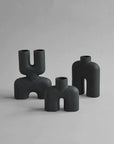 Three quirky vases, including the 101Cph Cobra Uno Mini Black 203024 by 101 Copenhagen, in black color, placed on a grey surface.