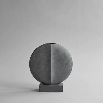 A 101Cph Guggenheim Mini Dark Grey 203005 concrete vase on a grey background, inspired by the Cobra Arts Movement, by 101 Copenhagen.