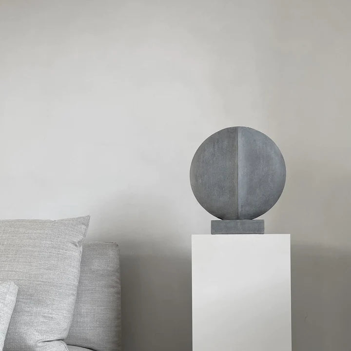 A 101Cph Guggenheim Mini Dark Grey 203005, reminiscent of the Cobra Arts Movement, sitting on a pedestal in a living room. (Brand Name: 101 Copenhagen)