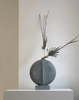 A concrete sculpture with a palm tree on top of it, inspired by the Cobra Arts Movement. This product is called the 101Cph Guggenheim Mini Dark Grey 203005 and is made by the brand 101 Copenhagen.