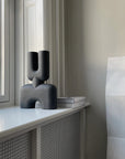 A black 101Cph Cobra Double Medio Black 212006 vase sits on top of a window sill.