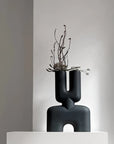 A black 101Cph Cobra Double Medio Black 212006 vase sits on top of a white pedestal.