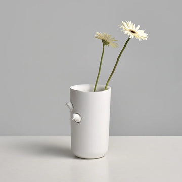 The Haoshi Sparrow Vase M, a luxurious symbol of opulence, holds a delicately arranged flower within its pristine white exterior.