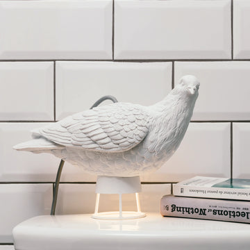 A peaceful white Lamp Haoshi Dove X Light 02 perched delicately on a table, bringing delight next to a book.